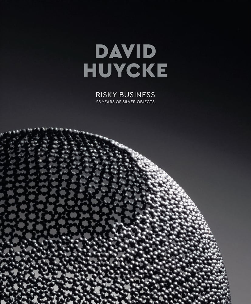 Portion of silver sphere with hole to top, made of small ball bearings, grey cover, David Huycke in grey font above