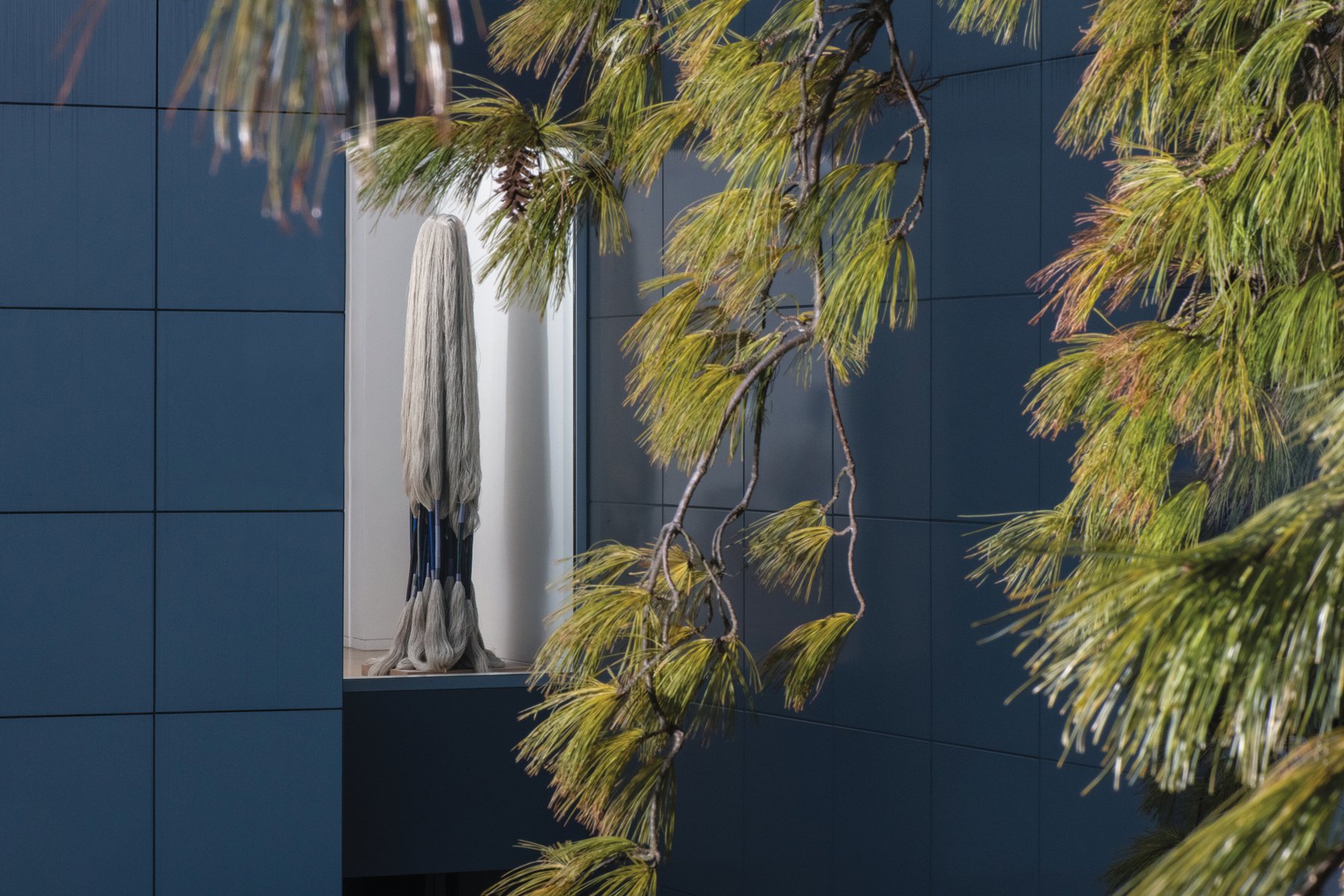 Sculpture of bird made from wood and fibres, on white windowsill looking out, The Grotta Home by Richard Meier in white font to upper left.