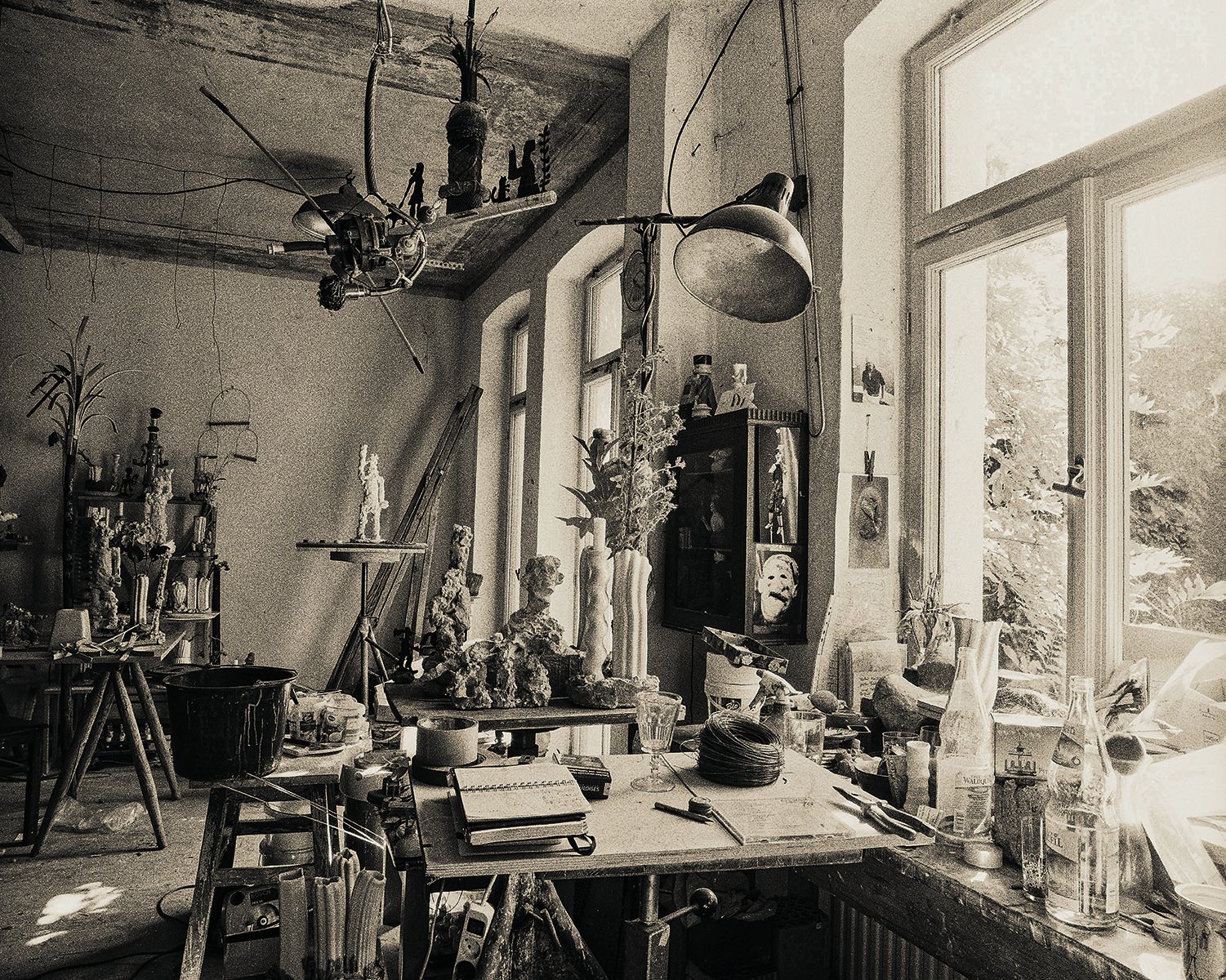 Black and white interior of artist studio, sculpture head on table, INSIGHTS INTO 19 ATELIERS PHOTOGRAPHY BY SIBYLLE MANIA in white font above.