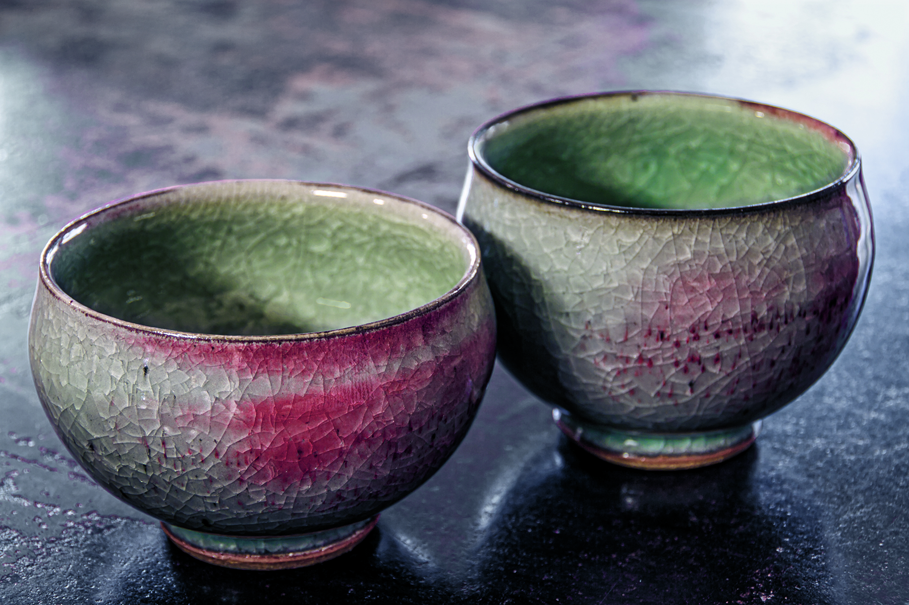 Pale blue ceramic bowl with orange markings, on white surface, YOUNG-JAE LEE DAS GRUN IN DEN SCHALEN in white font to upper right.