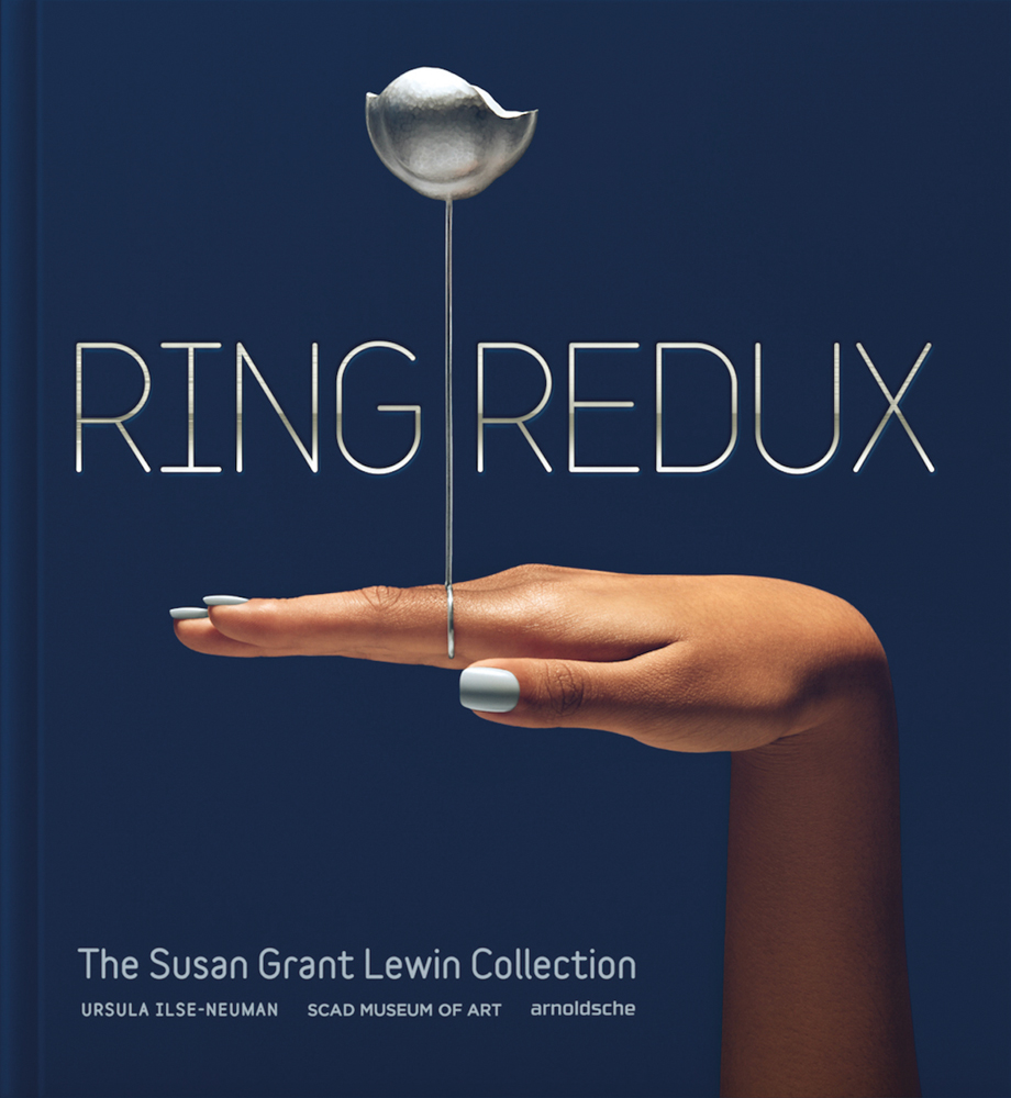 Dark-skinned hand with silver ring with long stem and flower, on index finger, on cover of 'Ring Redux, The Susan Grant Lewin Collection', by Arnoldsche Art Publishers.