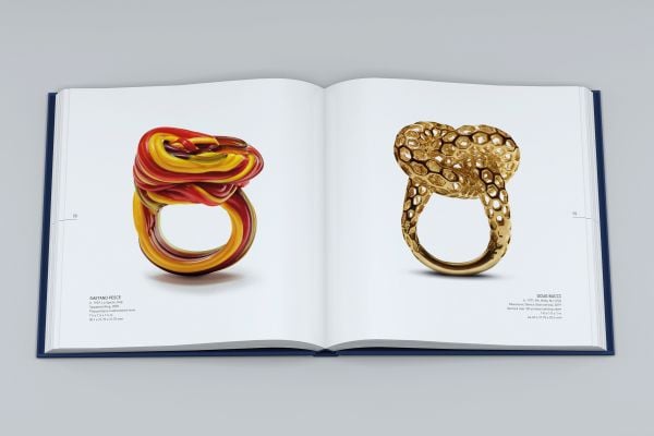 Dark-skinned hand with silver ring with long stem and flower, on index finger, on cover of 'Ring Redux, The Susan Grant Lewin Collection', by Arnoldsche Art Publishers.