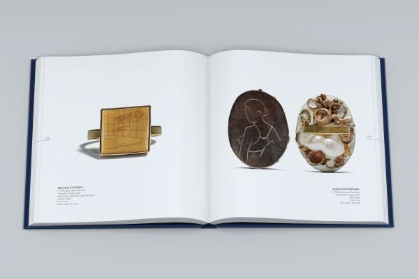 Dark-skinned hand with silver ring with long stem and flower, on index finger, on cover of 'Ring Redux, The Susan Grant Lewin Collection', by Arnoldsche Art Publishers.