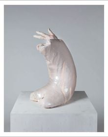 Deformed head like sculpture with ears glazed in white and pink sitting on fabric covered box, on cover of 'Erwin Wurm, Dissolution', by Arnoldsche Art Publishers.
