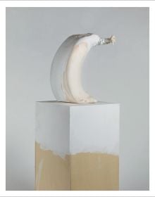 Deformed head like sculpture with ears glazed in white and pink sitting on fabric covered box, on cover of 'Erwin Wurm, Dissolution', by Arnoldsche Art Publishers.