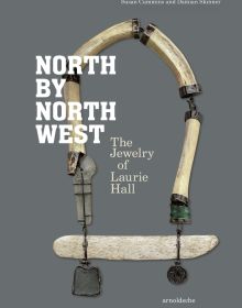 Long jewelry piece made of wooden tube shapes, and dark metal pendants on grey cover of 'North by Northwest, The Jewelry of Laurie Hall', by Arnoldsche Art Publishers.