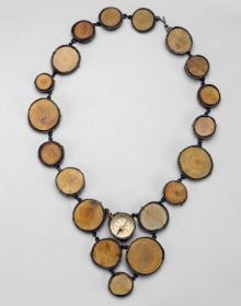 Book cover of North by Northwest, The Jewelry of Laurie Hall, with a jewelry piece made of wooden tube shapes, and dark metal pendants. Published by Arnoldsche Art Publishers.