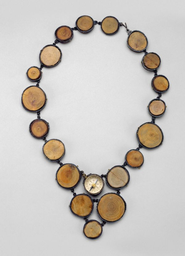 Book cover of North by Northwest, The Jewelry of Laurie Hall, with a jewelry piece made of wooden tube shapes, and dark metal pendants. Published by Arnoldsche Art Publishers.