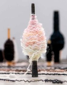 Book cover of Kari Steihaug, with a spinning spool bound with wavy wool in pastel colours. Published by Arnoldsche Art Publishers.