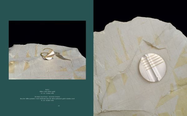 Blue book cover of Gerti Machacek, Jewellery Sculpture, featuring an oxidised copper jewellery piece, shaped like an eye, with eyelashes. Published by Arnoldsche Art Publishers.