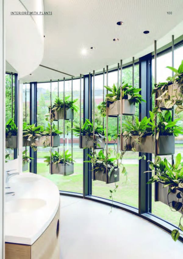 Seated figure with laptop, bright spot light, surrounded by multicoloured leaf shapes, on white cover of 'Plants at Work, An inspirational guide to greenterior design', by Avedition Gmbh.