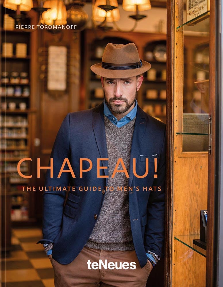 Book cover of Chapeau! The Ultimate Guide to Men's Hats, with a man wearing fedora hat, navy jacket and brown trousers. Published by teNeues Books.