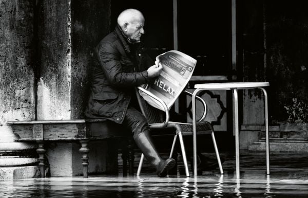 Book cover of Venezia: Through A Venetian's Eye, with a view under arched building of canal in Venice with a man throwing beer barrel in air. Published by teNeues Books.