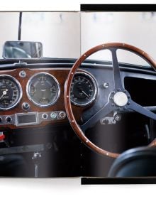 Book cover of The Aston Martin Book, with the front end of silver Aston Martin DB5 with headlights on. Published by teNeues Books.