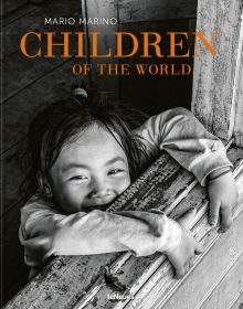 Small child smiling up at camera, arms and hands clutching window ledge, Children of the World in orange font above, by teNeues Books.