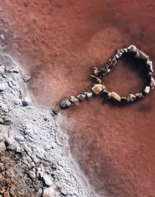 Aerial shot of pink waters of Lake Lemuria, white salt coastline, THE BEAUTY OF UKRAINE LANDSCAPE PHOTOGRAPHY in white, and black font above.