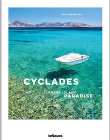 Bright blue and pale green sea of Greek island, small white boat floating to lower right, on white cover, 'CYCLADES', in white font below.