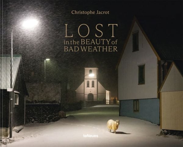Book cover of Lost in the Beauty of Bad Weather, with a sheep walking through snowy residential street at night. Published by teNeues Books.