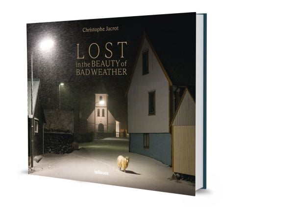 Book cover of Lost in the Beauty of Bad Weather, with a sheep walking through snowy residential street at night. Published by teNeues Books.