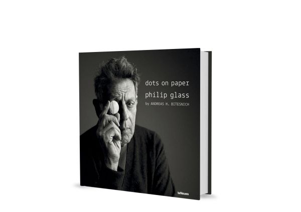 Book cover of dots on paper, Philip Glass by Andreas H. Bitesnich, with the composer in dark jacket, holding circular piece of glass to right eye. Published by teNeues Books.