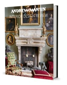 Interior living room of La Maison Semonville with stone fireplace, framed paintings and plush furniture, on cover of 'Andrew Martin Interior Design Review Vol. 27', by teNeues Books.