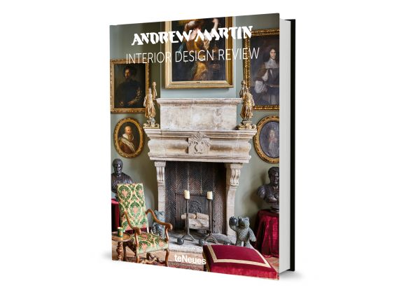 Interior living room of La Maison Semonville with stone fireplace, framed paintings and plush furniture, on cover of 'Andrew Martin Interior Design Review Vol. 27', by teNeues Books.