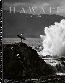 Book cover of Olaf Heine's Hawaii, with surfer standing on rocks holding surf board near the crashing waves of the sea. Published by teNeues Books.