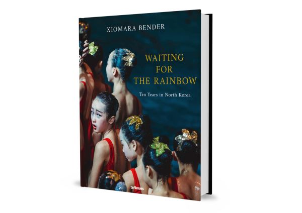 Book cover of Xiomara Bender's Waiting for the Rainbow: Ten Years in North Korea, with a group of dancers lining up in red costumes. Published by teNeues Books.