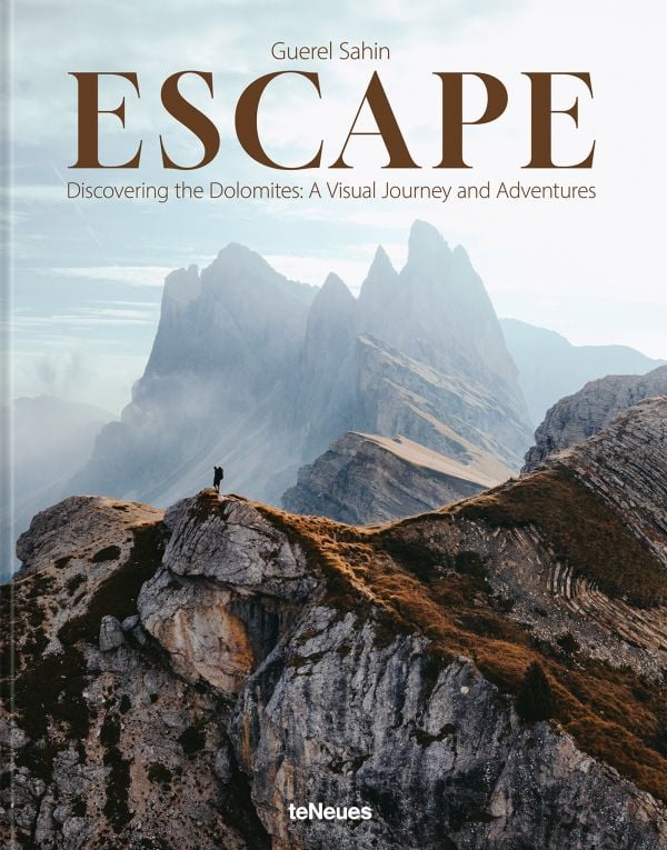 Book cover of Escape: Discovering the Dolomites: A Visual Journey and Adventures; featuring an adventurer standing on top of the Dolomite Mountains. Published by teNeues Books.