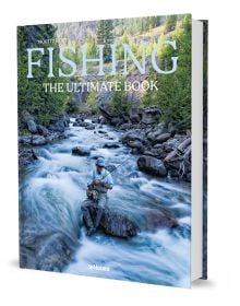 Book cover of Fishing: The Ultimate Book, with a fisherman sitting on a rock in the middle of a fast flowing river. Published by teNeues Books.
