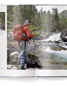 Book cover of Fishing: The Ultimate Book, with a fisherman sitting on a rock in the middle of a fast flowing river. Published by teNeues Books.