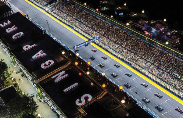 Book cover of The Stylish Life: Grand Prix, featuring a model in 60s clothes standing on race track with car and driver behind. Published by teNeues Books.