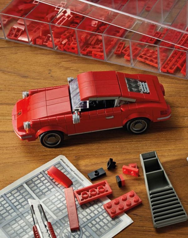 Side profile of three Porsche LEGO models in red, black and white, on cover of 'Porsche 911, Legends Made of LEGO®', by HEEL.