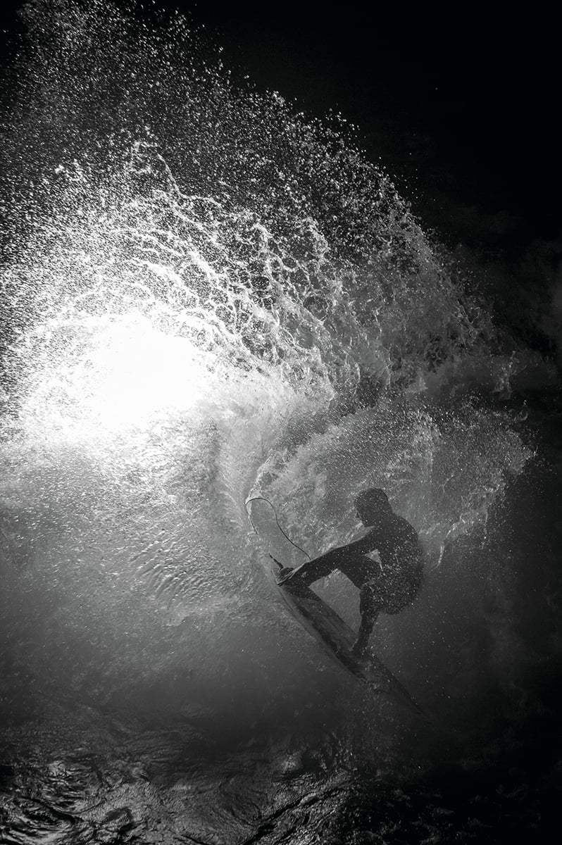 Reflection of male surfer on sand carrying surfboard, The Other Side of Surfing in white font to centre.