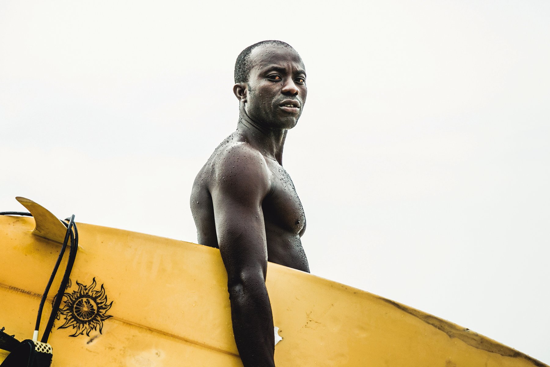 Reflection of male surfer on sand carrying surfboard, on cover of 'The Other Side of Surfing', by Galindo Publishing.