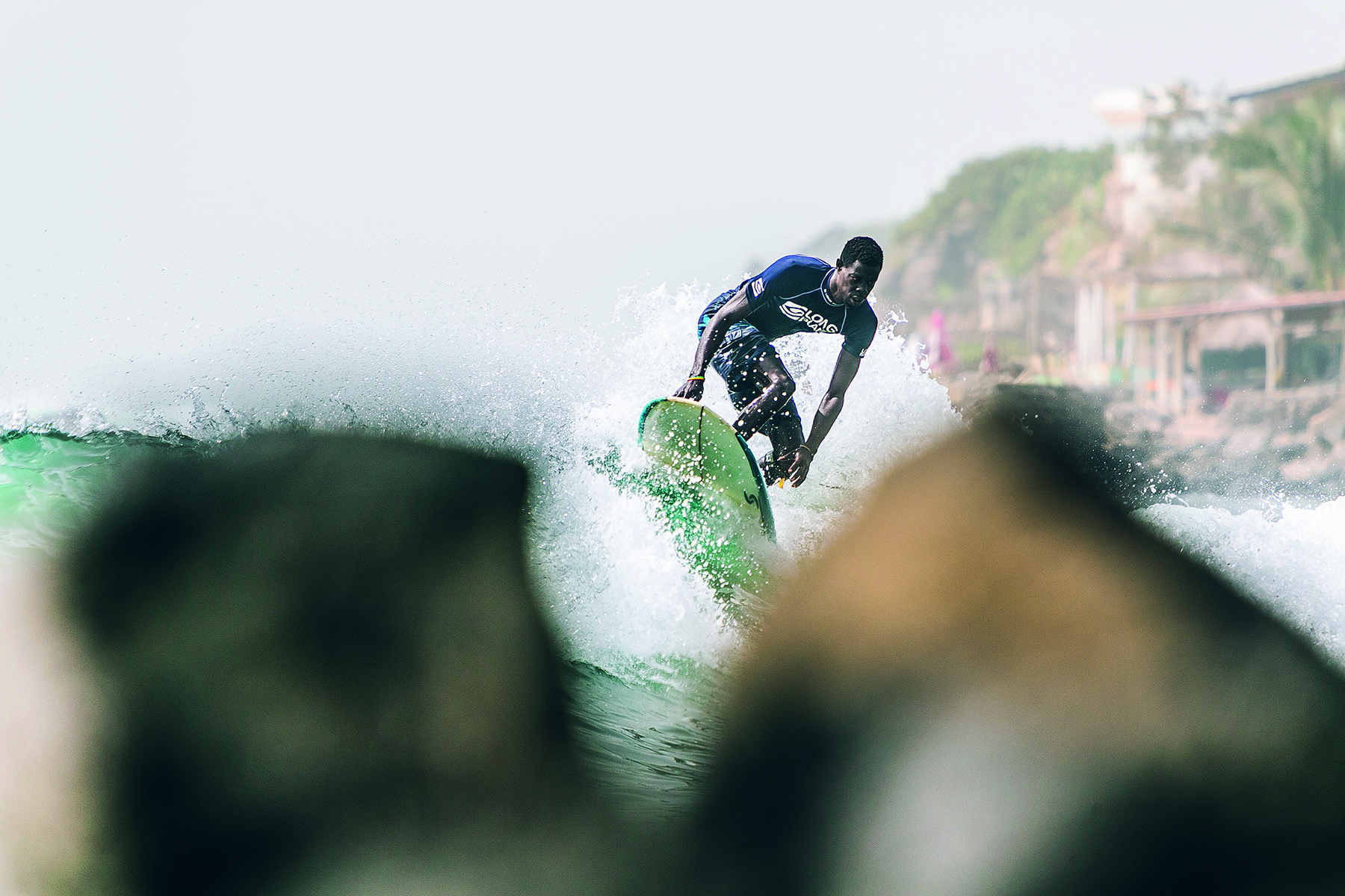 Reflection of male surfer on sand carrying surfboard, The Other Side of Surfing in white font to centre.