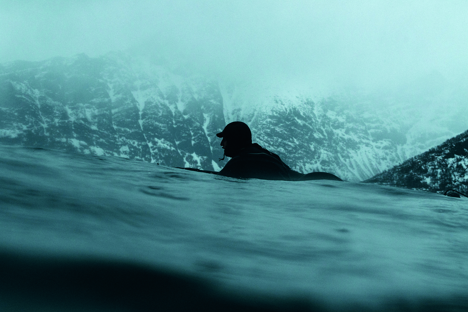 Reflection of male surfer on sand carrying surfboard, The Other Side of Surfing in white font to centre.