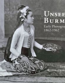 Burmese woman in traditional dress, sitting on rug, hand on cushion, on cover of 'Unseen Burma, Early Photography 1862-1962', by River Books.