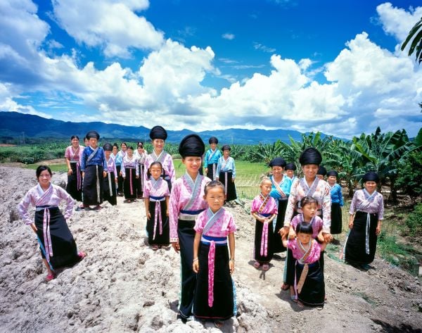 Book cover of Tai: A Woven Culture, with rice fields with workers in colourful clothes smiling at camera. Published by River Books.
