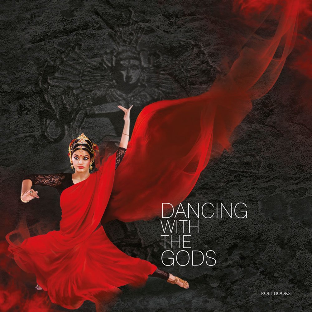 Indian dancer Sohini Roychowdhury in red robes in expressive dance posse on black and grey patterned cover with Dancing With The Gods in fine white font