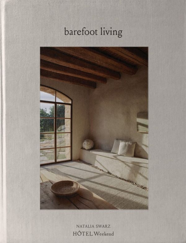 Book cover of Barefoot Living; featuring a rustic, minimalist interior with arch window and ceiling beams. Published by Helmin & Sorgenfri.