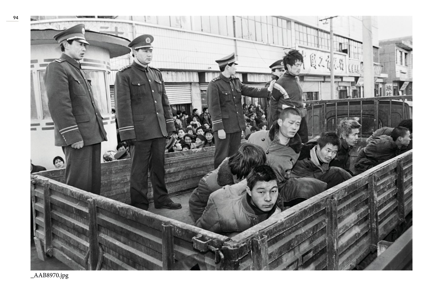 Chained feet of prisoner in flipflops playing game with pebbles and white cloth on floor, NIU GUOZHENG GAMBLING WITH LIFE in brown and white font on left beige banner.