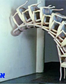 Installation sculpture of long spouted metal jugs fixed together, Germano Celant ARMAN 1955 1974 in black and blue font above.