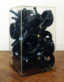 Installation sculpture of long spouted metal jugs fixed together, Germano Celant ARMAN 1955 1974 in black and blue font above.