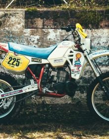 Head of biker with red helmet, peak visor and goggles, dark blue cover, Deus Ex-Machina SWANK RALLY in off white font near centre