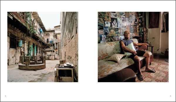 Front of old Cuban house, tropical green foliage growing up around door frame, CUBA VIVIR CON in gold font on blue banner above.