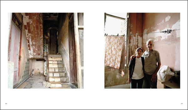 Front of old Cuban house, tropical green foliage growing up around door frame, CUBA VIVIR CON in gold font on blue banner above.