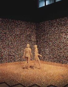 3 figures huddled in corner of blue fabric covered room, blue sculpture in foreground, white snowflakes, SANDY SKOGLUND in white font above