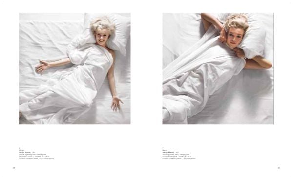 Marilyn Monroe in playful pose, laying beneath a white sheet on bed, Douglas Kirkland in black font to upper left.