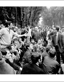 Shot of wet brick roads of Milan in rain, surrounded by buildings, CESARE COLOMBO Fotographie Photographs 1952-2012 in yellow and white font to centre right.